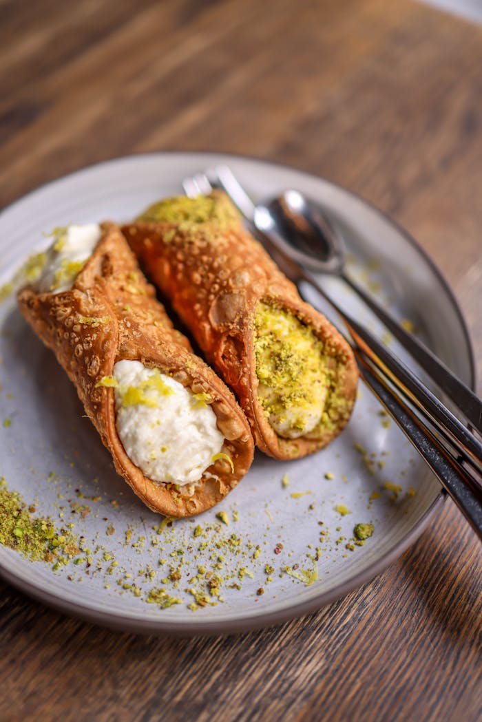 Close-up of two crispy cannoli on a plate filled with ricotta and topped with pistachios.