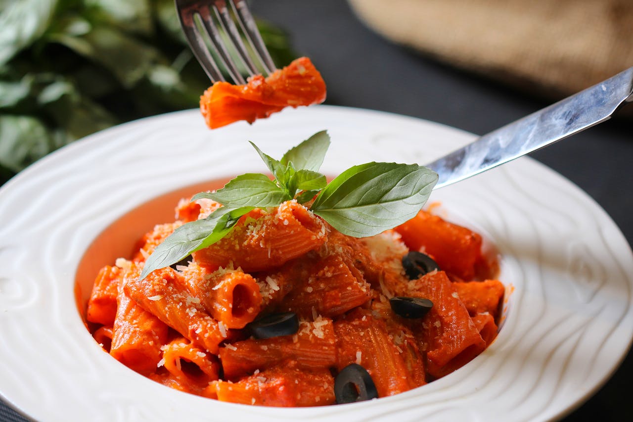Delicious rigatoni pasta with tomato sauce, olives, and fresh basil, perfectly captured in a food photography shot.
